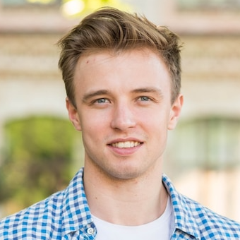 A young man wearing a blue and white checkered shirt is smiling for the camera.