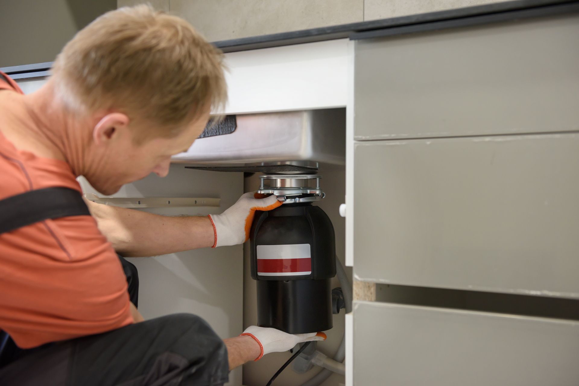 A man is fixing a garbage disposal under a sink in a kitchen.