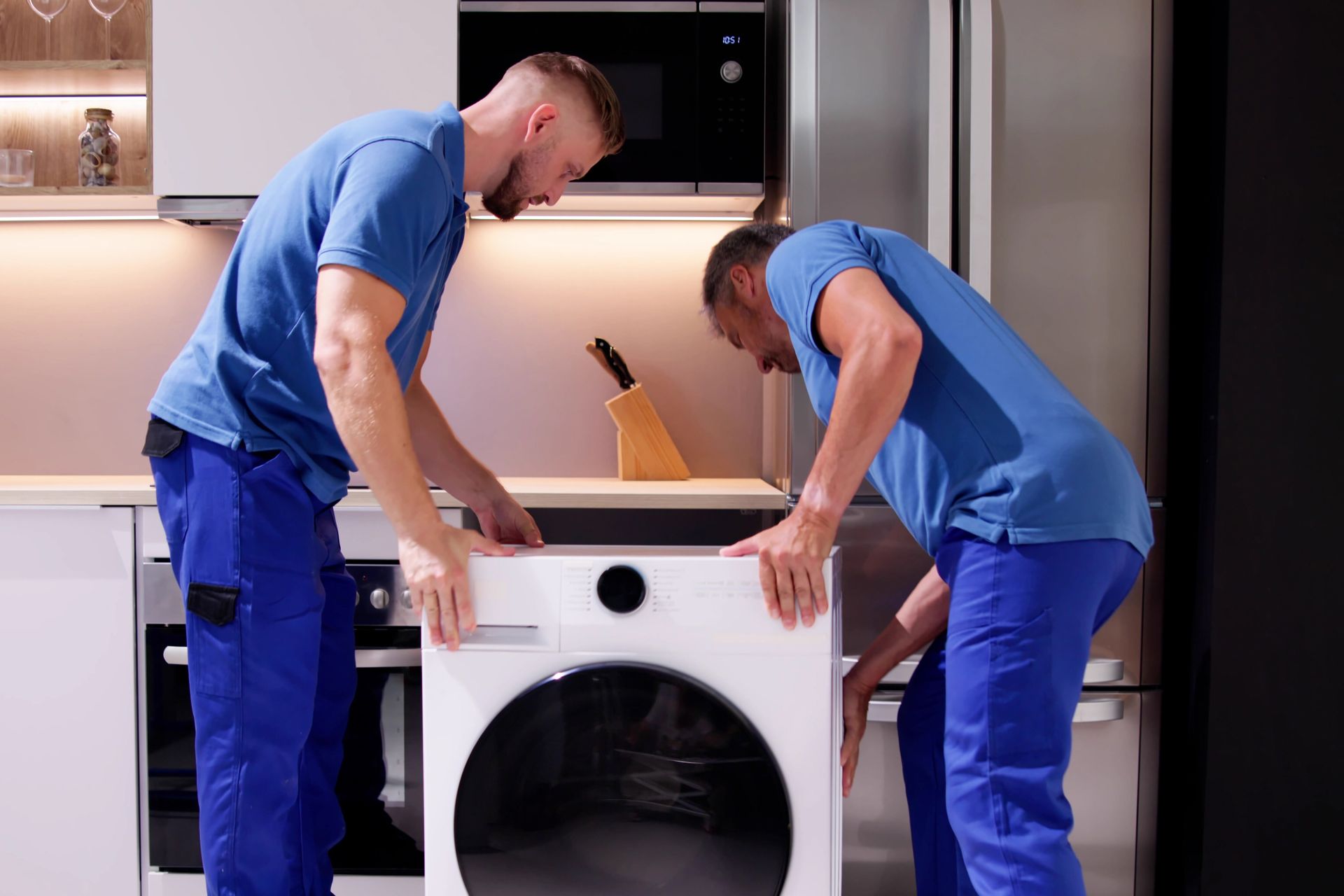 Two men are installing a washing machine in a kitchen.