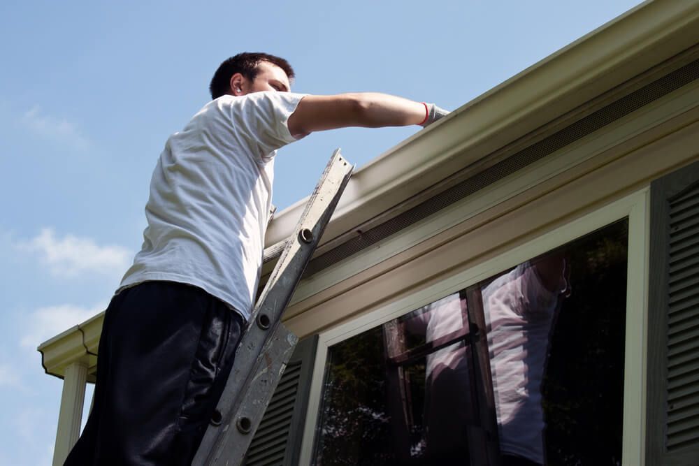 A Man on a Ladder is Working on the Gutters of a House — All-Clear Gutter Guard NQ in Cairns, QLD