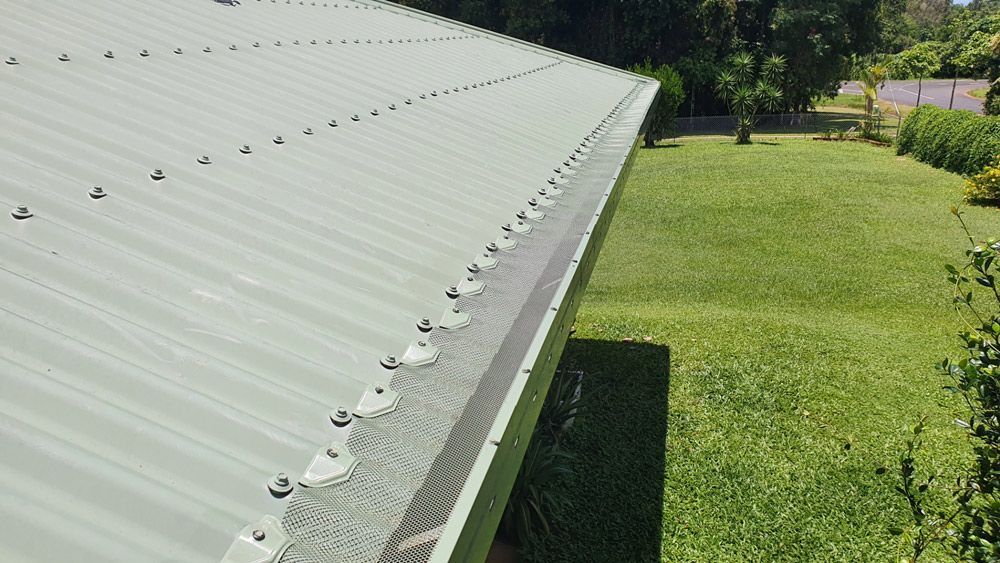 A Gutter on The Side of A Roof Next to A Lush Green Field — All-Clear Gutter Guard NQ in Cairns, QLD