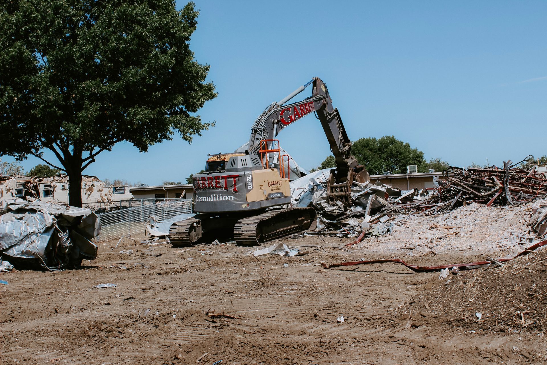 A large excavator is destroying a building in a field.