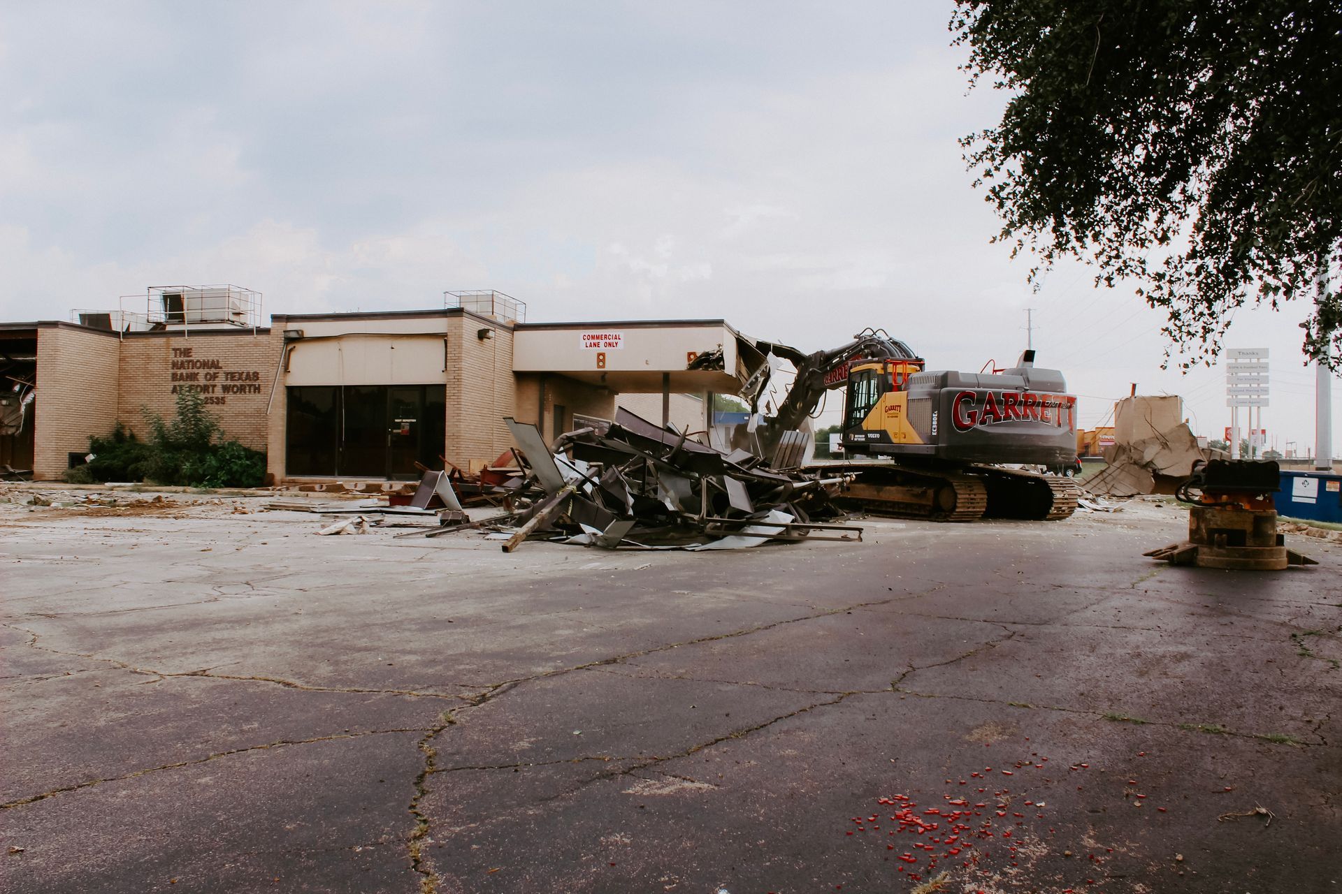 A large excavator is demolishing a building in a parking lot.