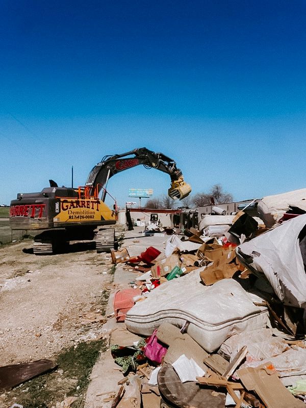 A large yellow excavator is working on a pile of trash.