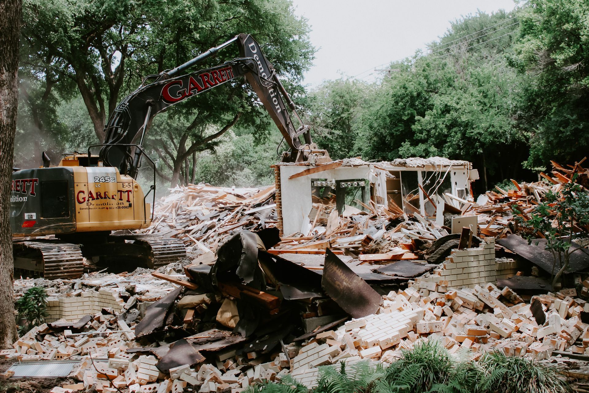 A large excavator is demolishing a house in the middle of a forest.