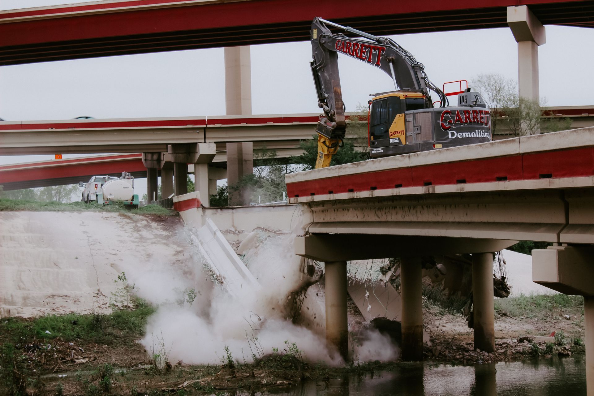 A large excavator is demolishing a bridge over a river.