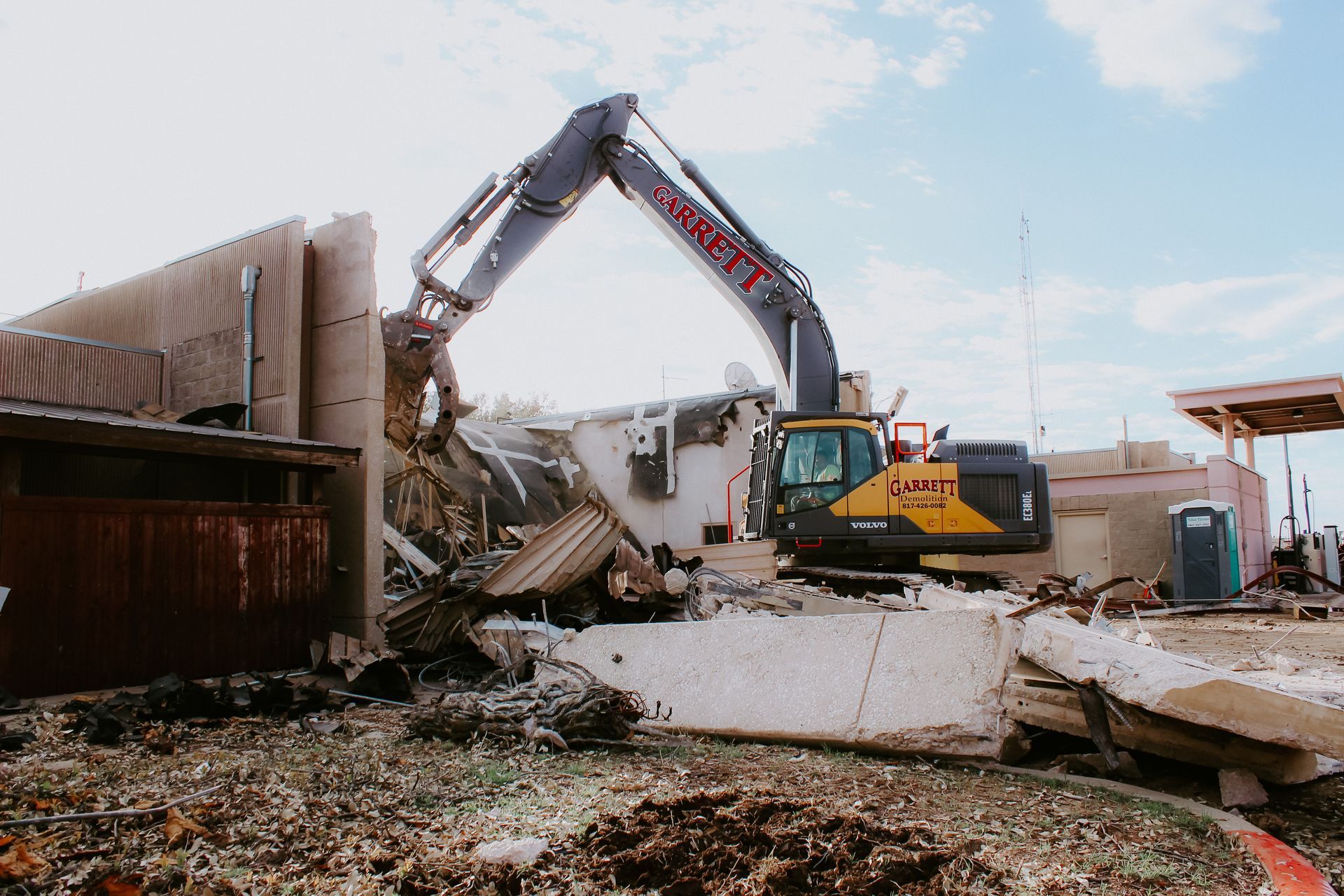 A large yellow excavator is demolishing a building.