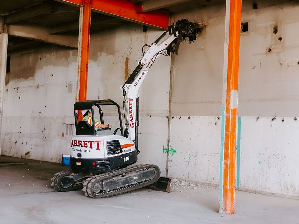 A small excavator is sitting in a warehouse next to a wall.