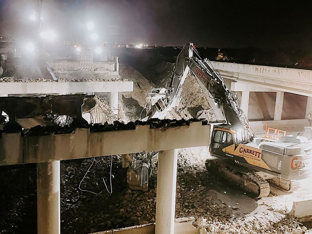 A large excavator is demolishing a bridge at night.