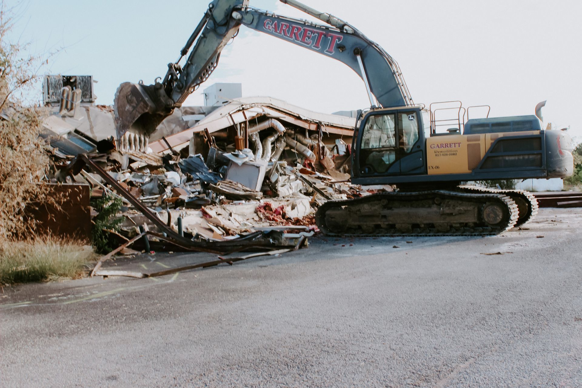 A large excavator is demolishing a building in a parking lot