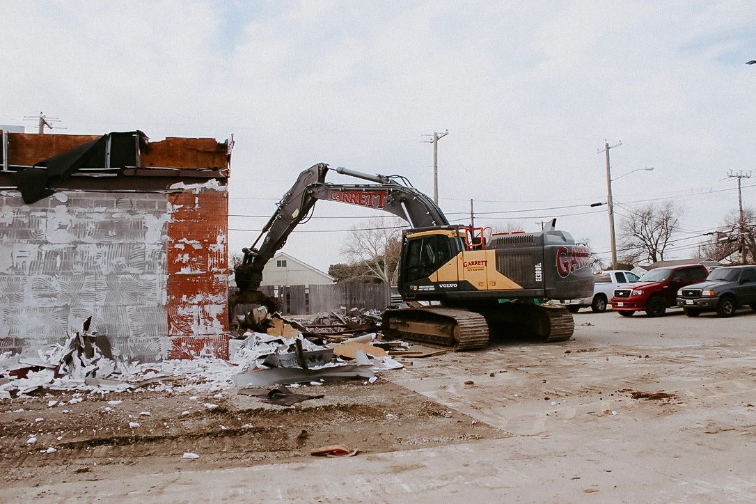 A bulldozer is demolishing a building in a parking lot.