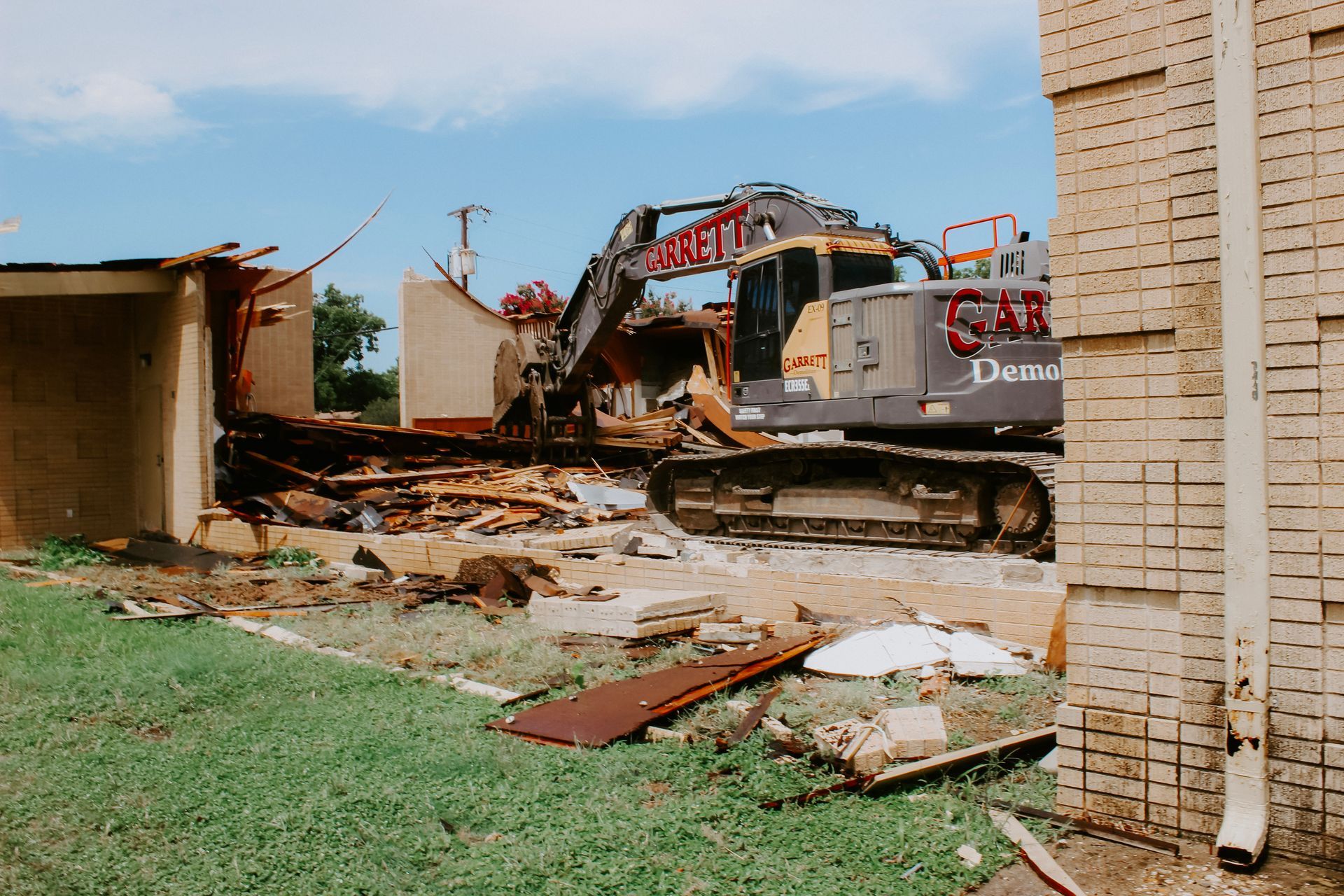 A large excavator is demolishing a brick building.