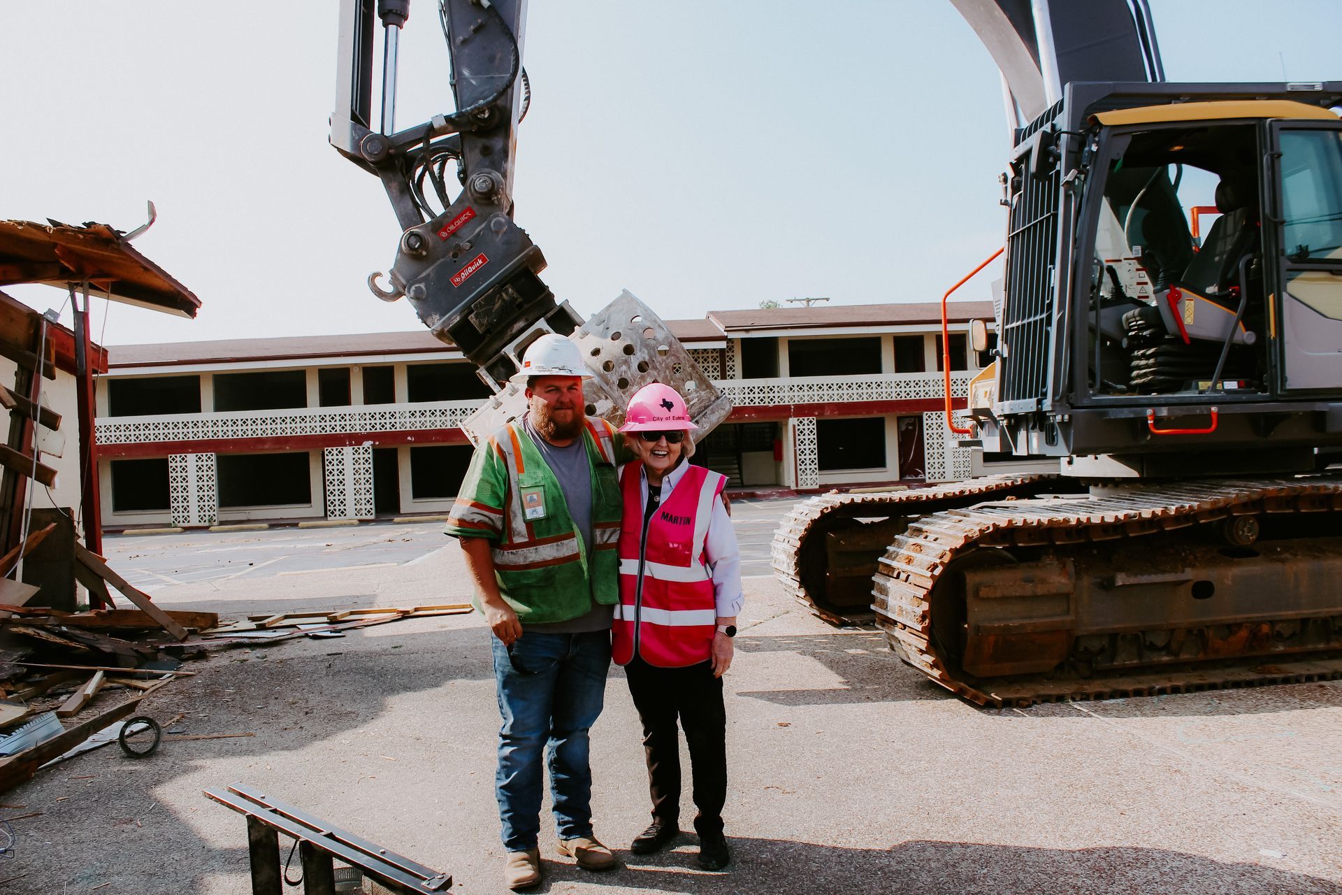 A man and a woman are standing in front of a large excavator.