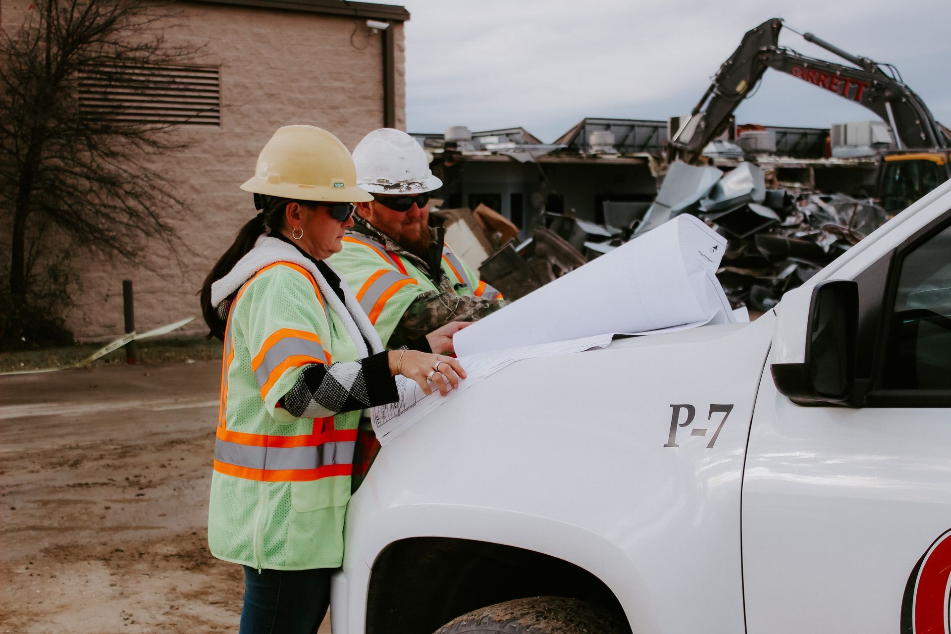 A man and a woman are standing next to a truck looking at blueprints.