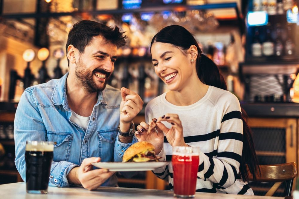 A man and a woman are sitting at a table in a restaurant eating hamburgers.