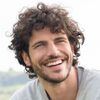 A man with curly hair and a beard is smiling.