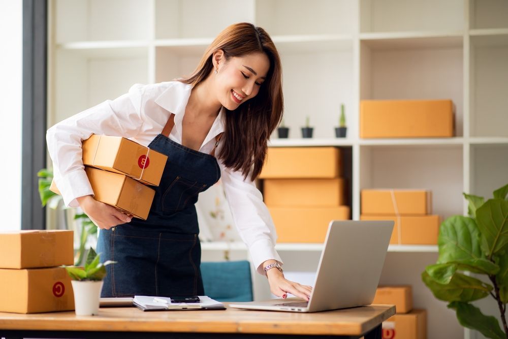 A woman is holding boxes and using a laptop computer.