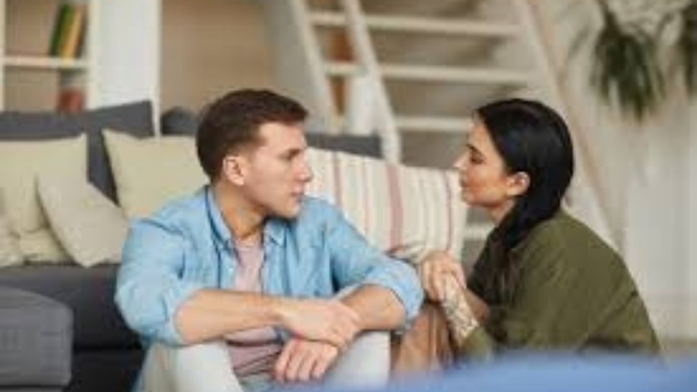 Man and woman sitting on floor, talking, serious expressions. Couch and ladder in background using communication skills from couples counseling.
