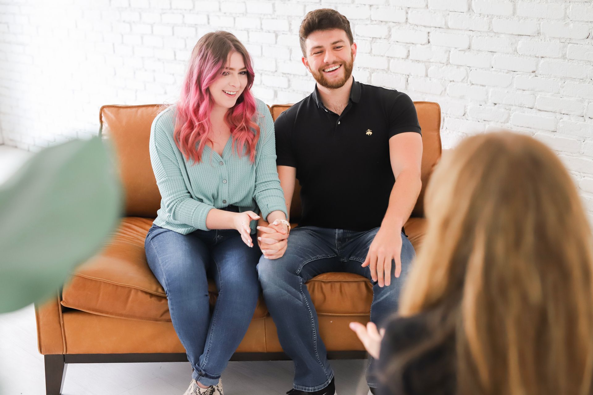 A man and a woman who are a couple are sitting on a couch holding hands in low cost counseling.