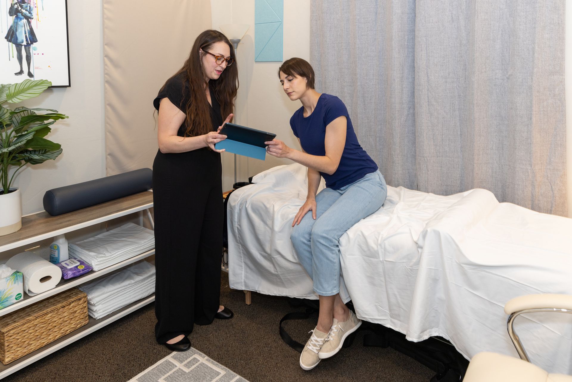 A Sound healing therapist assisting a woman sitting on a  Vibroacoustic Sound Therapy bed choosing from Solfeggio frequencies to experience sound frequency healing in Grapevine Texas. 