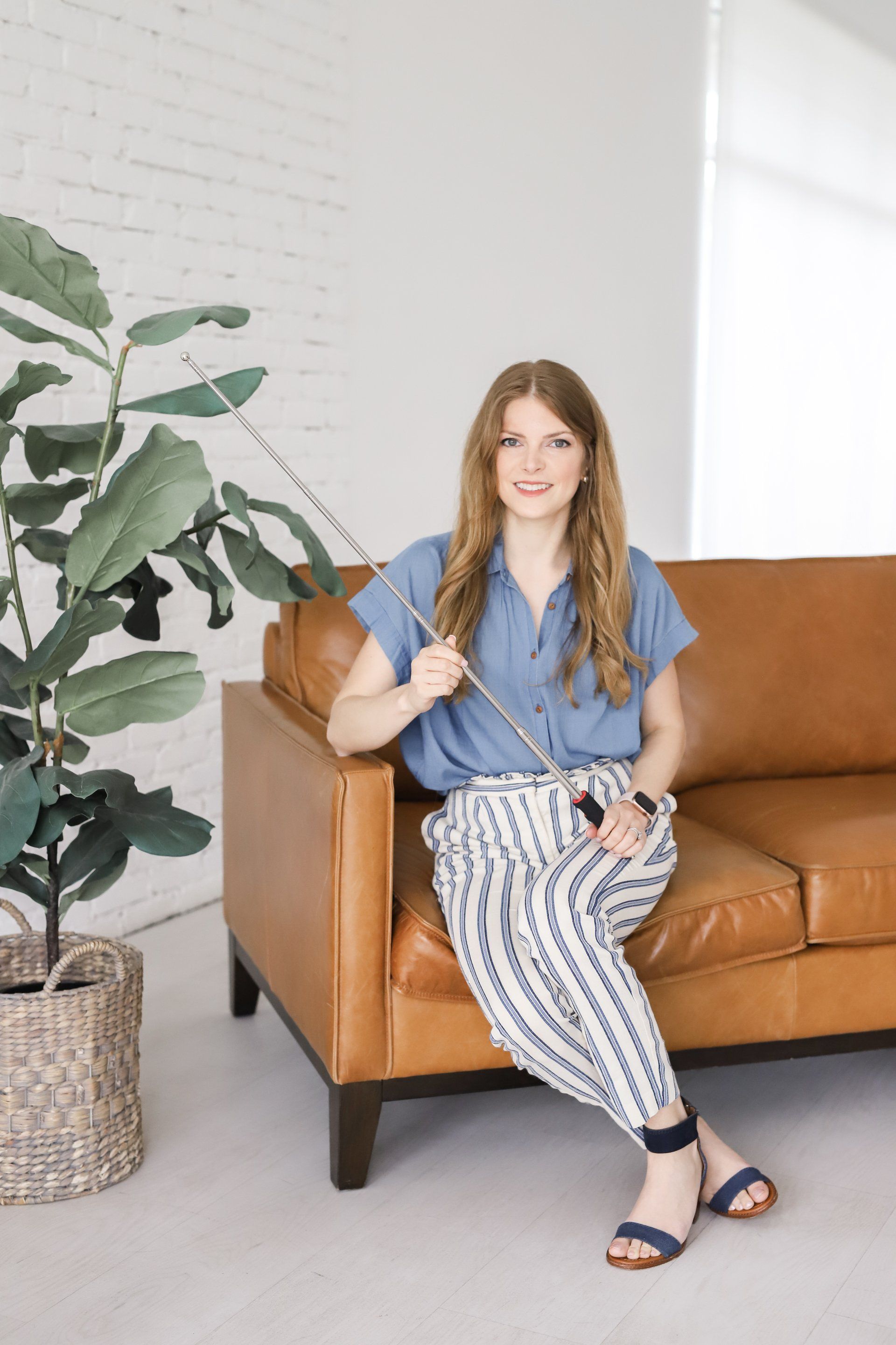A woman is sitting on a couch holding a stick.