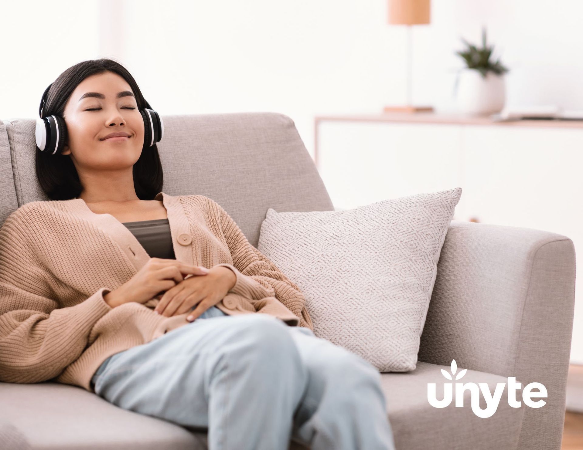 Person relaxing on a beige sofa with headphones, listening to rest and restoration protocol, eyes closed, in a bright living room