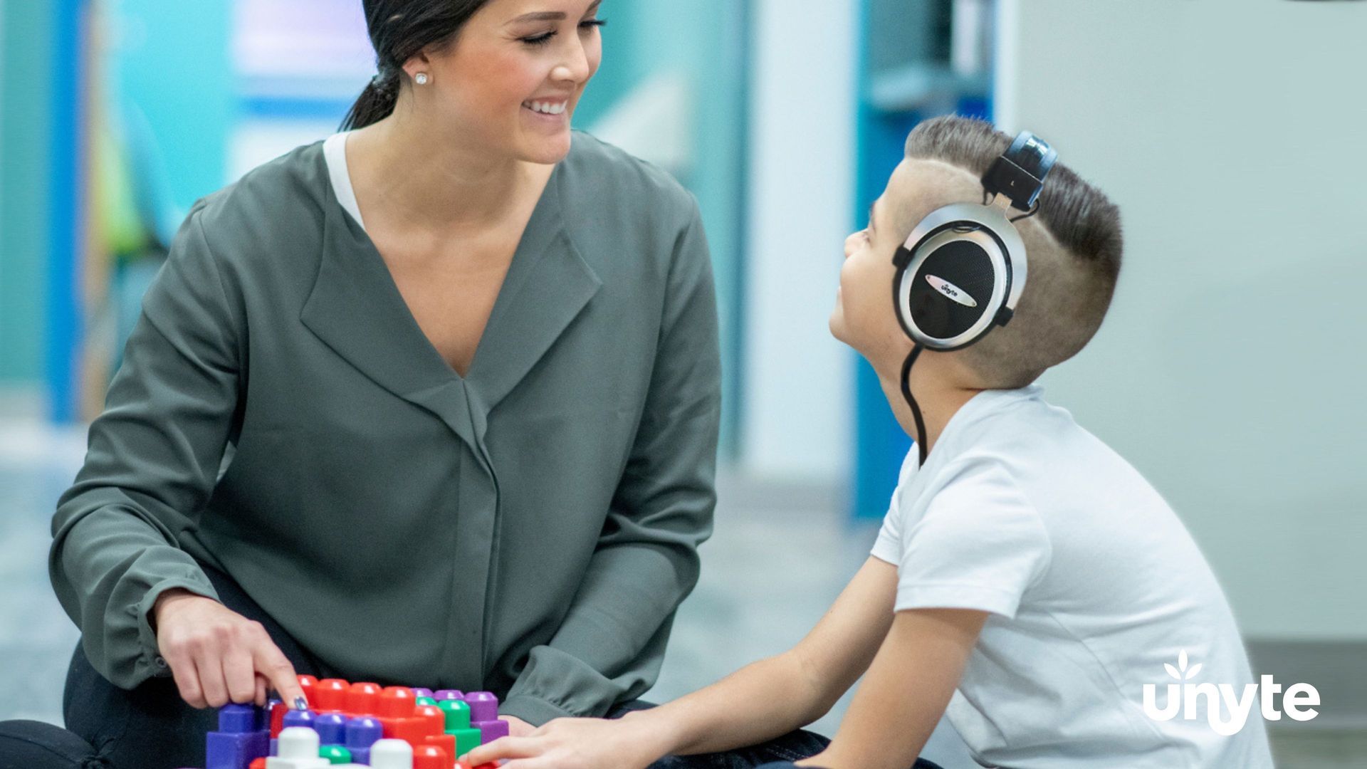 Woman and child wearing headphones listening to rest and restoration protocol play with colorful blocks in a bright classroom