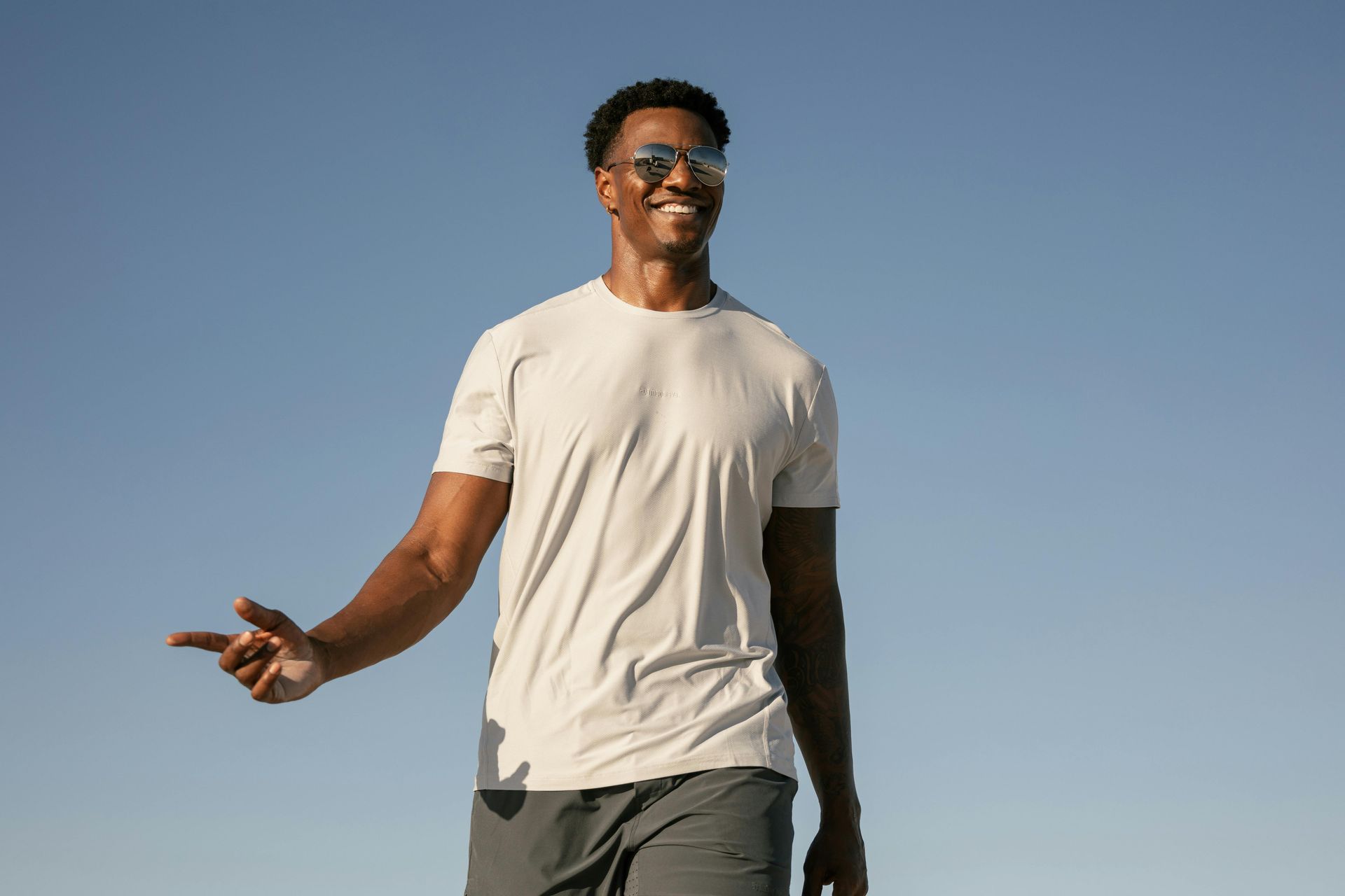 A man wearing sunglasses and a white t-shirt is standing in front of a blue sky smiling after healing from a counseling intensive in Grapevine Texas.