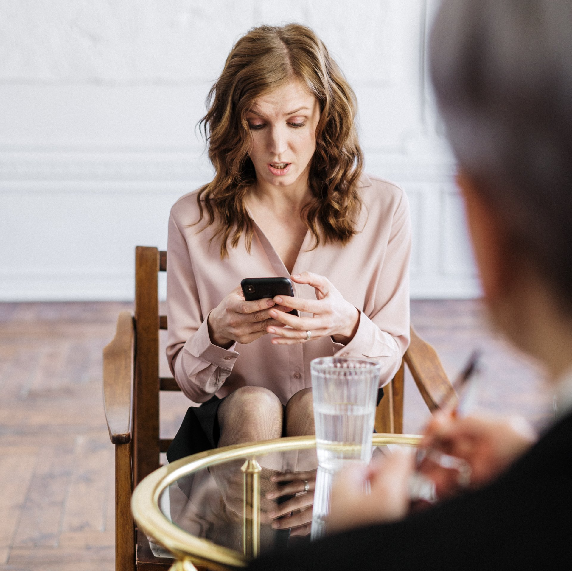A woman is sitting at a table looking at her phone participating in brain-body-based therapy in Texas. 