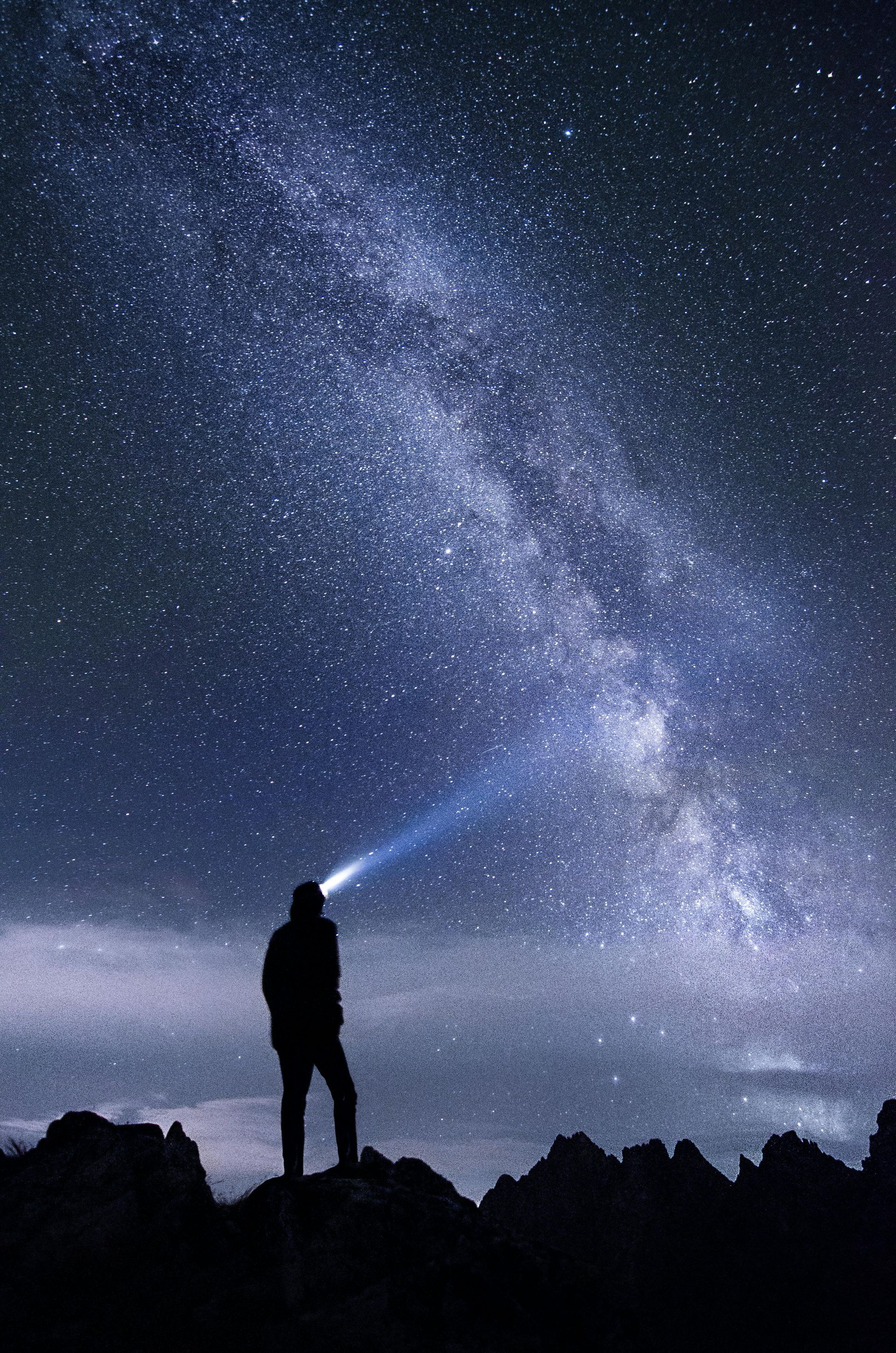 A person is standing on top of a mountain looking at the night sky with a flashlight. Deciding between EMDR and Brainspotting