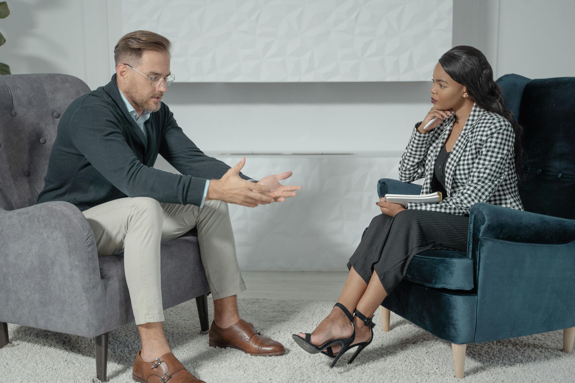 A man and a woman are sitting in chairs talking to each other participating in marriage counseling in DFW.