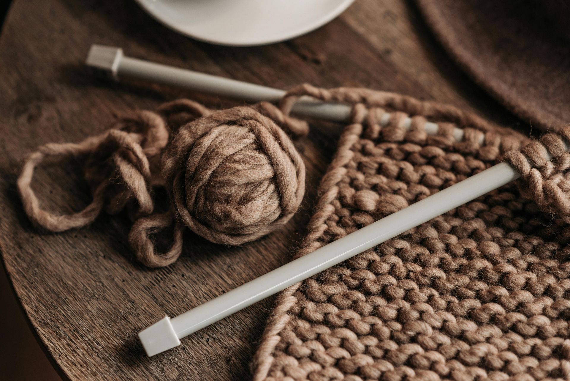 Knitted brown fabric with yarn balls and metal knitting needles on a rustic table to use bilateral stimulation for emotion regulation