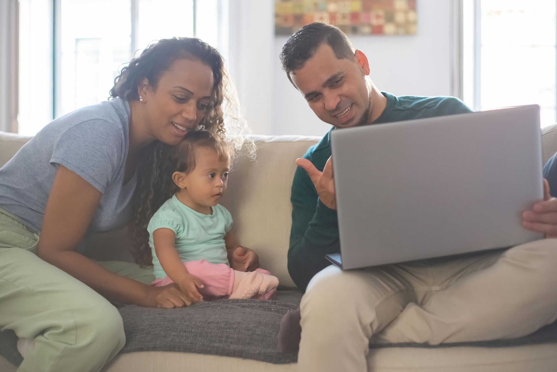 Three people on a couch looking at a laptop together in a bright living room receiving family counseling in Texas.