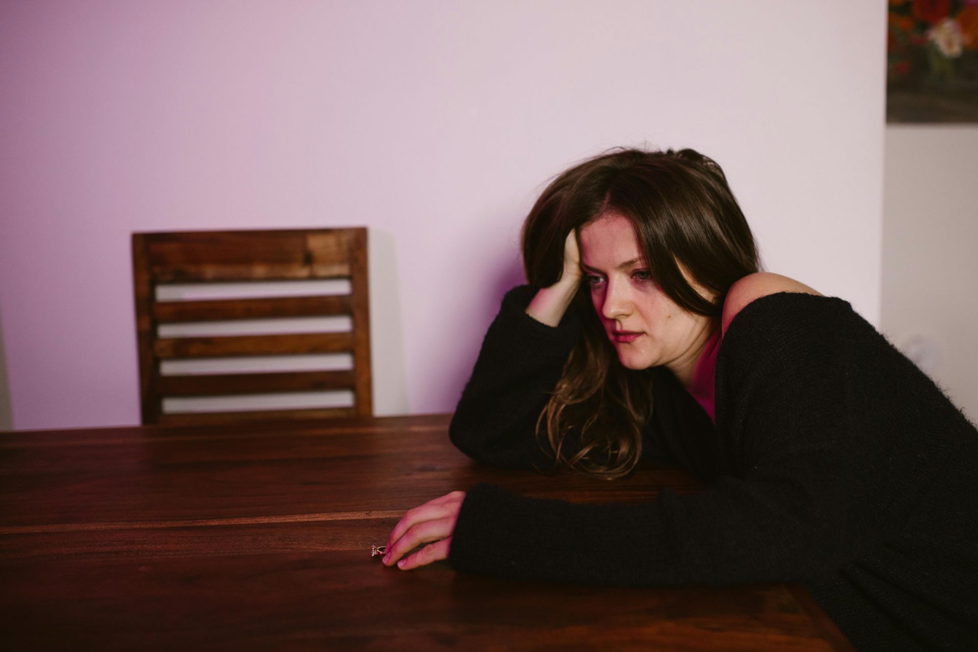 A woman is sitting at a table with her head resting on her hand.