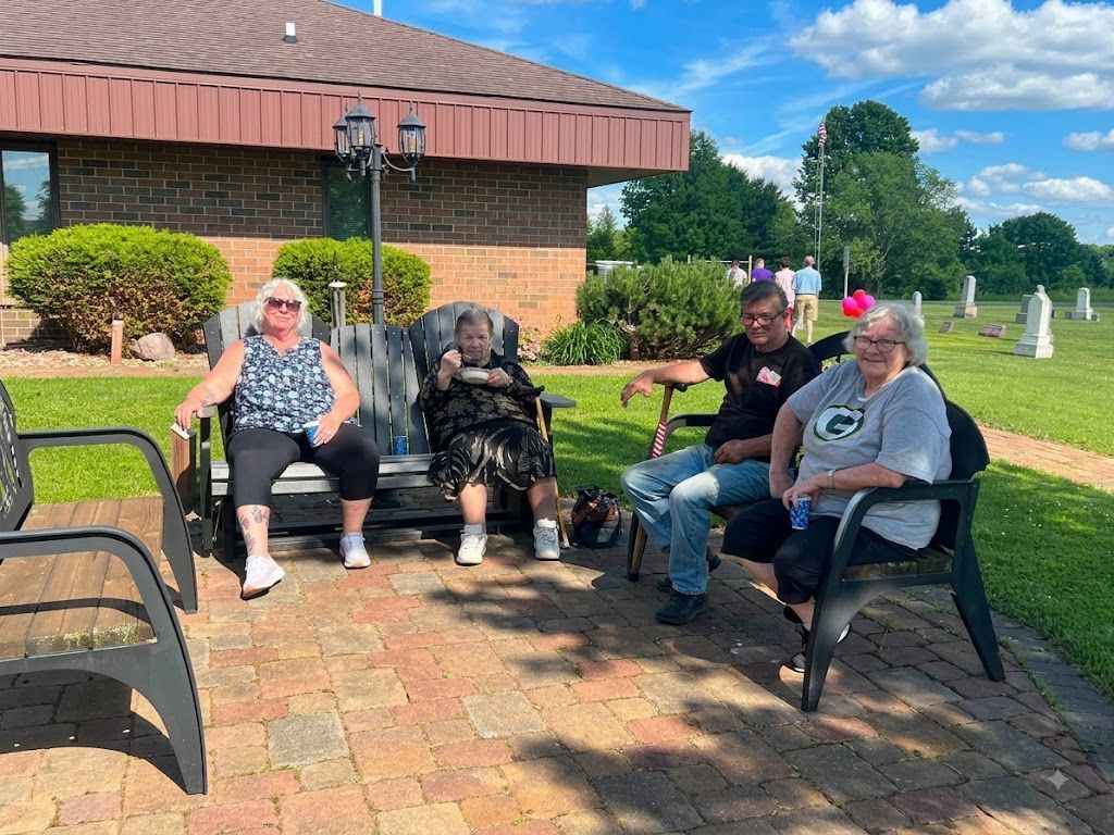 Four people sitting on benches outdoors beside a brick building on a sunny day.