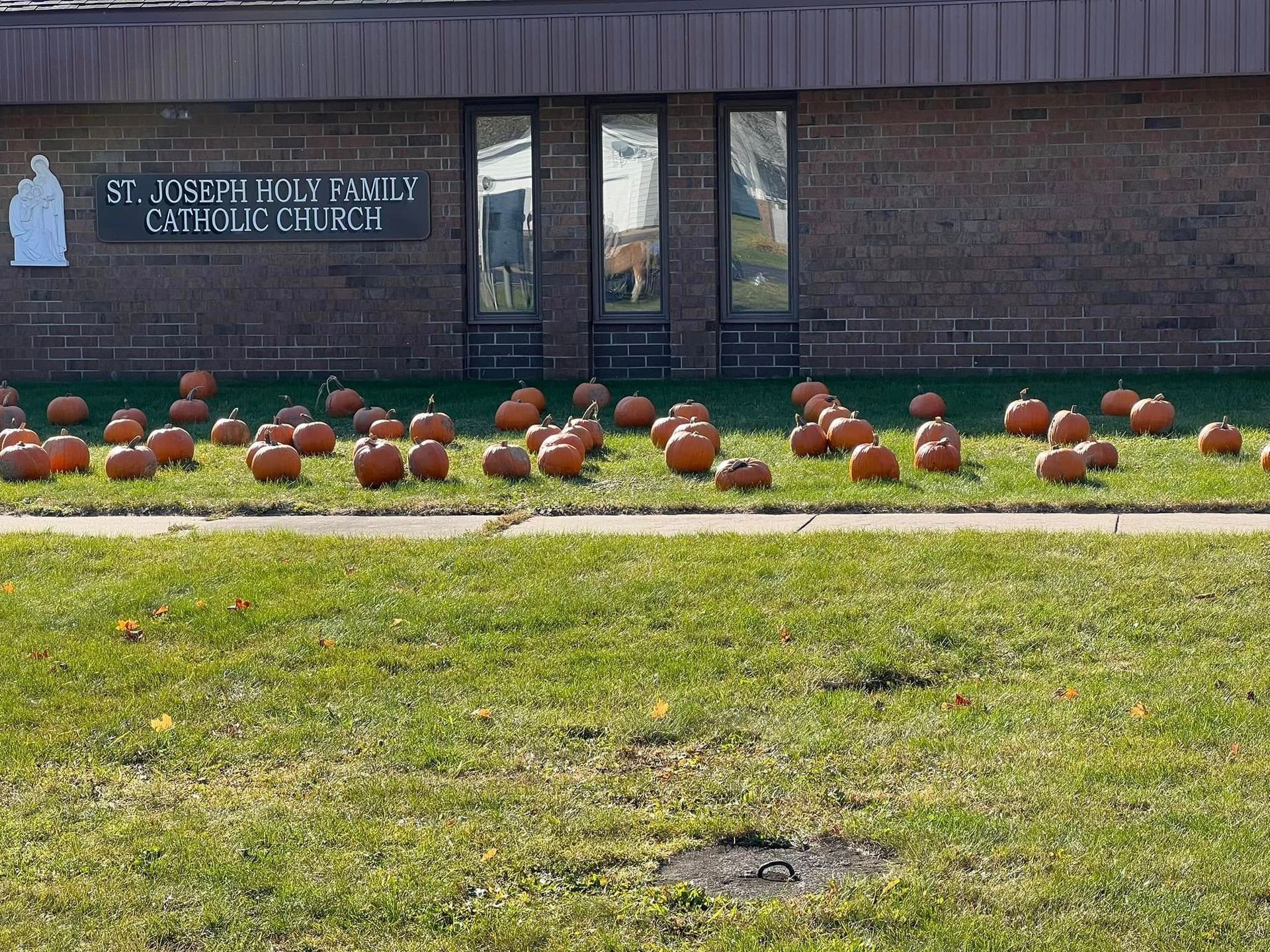 Brick school building with a sign and rows of orange pumpkins on the lawn.