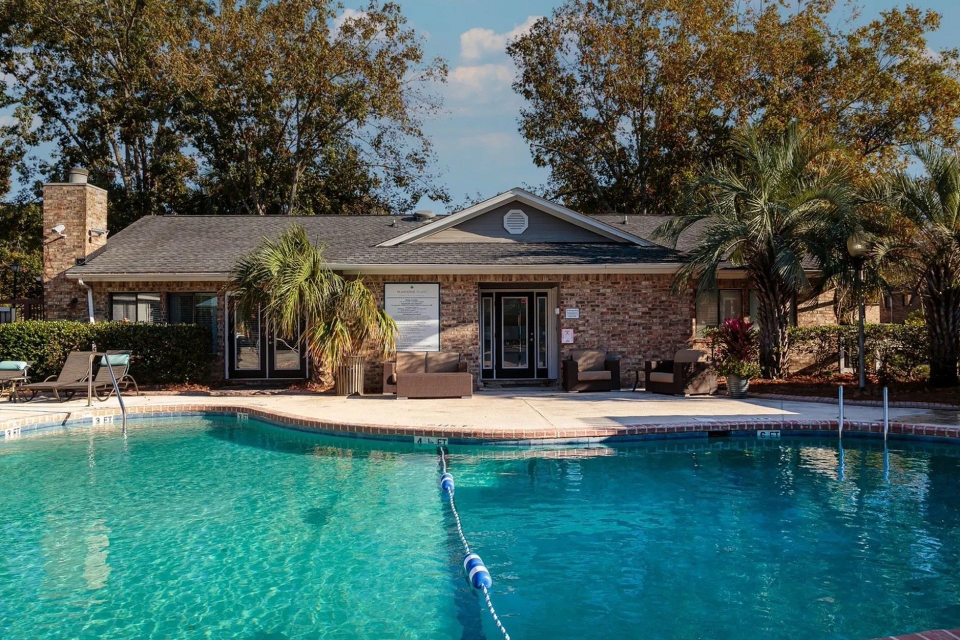A pool with turquoise water in front of a brick building with dark roof. Palm trees flank the building.