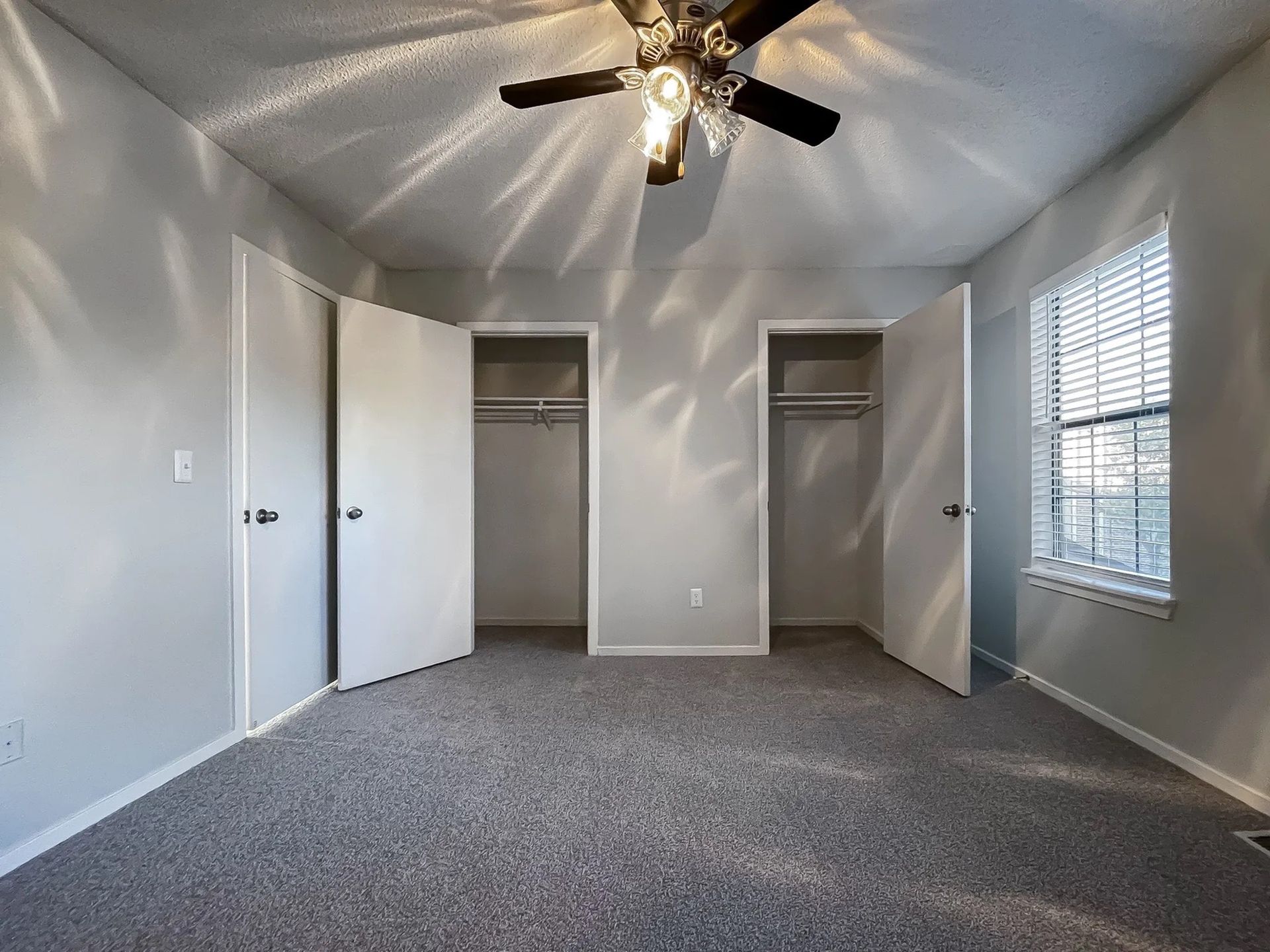 Empty bedroom with two closets, a ceiling fan, and a window with blinds.
