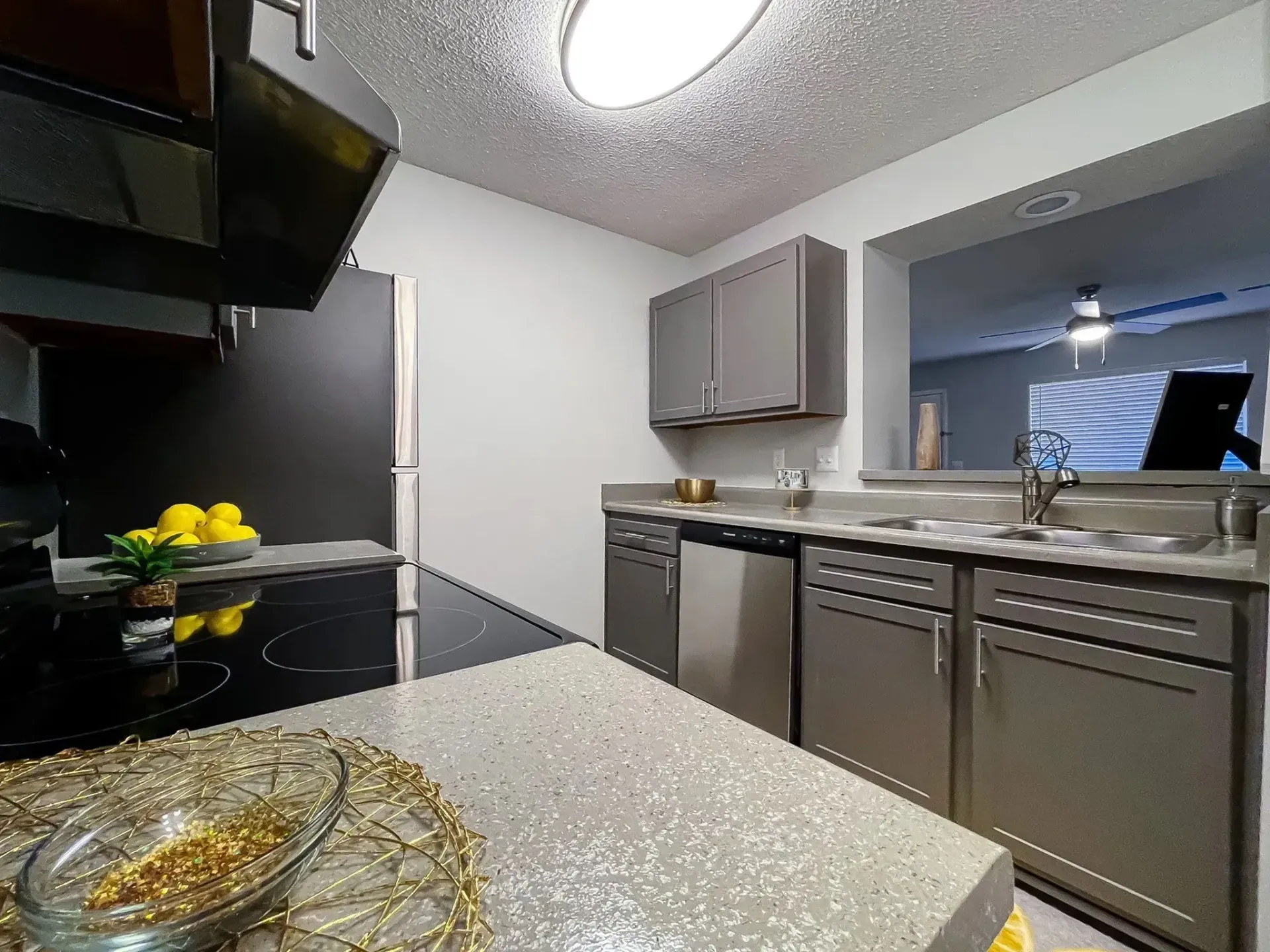 Modern kitchen with gray cabinets, speckled countertops, stainless steel appliances, and a pass-through window.