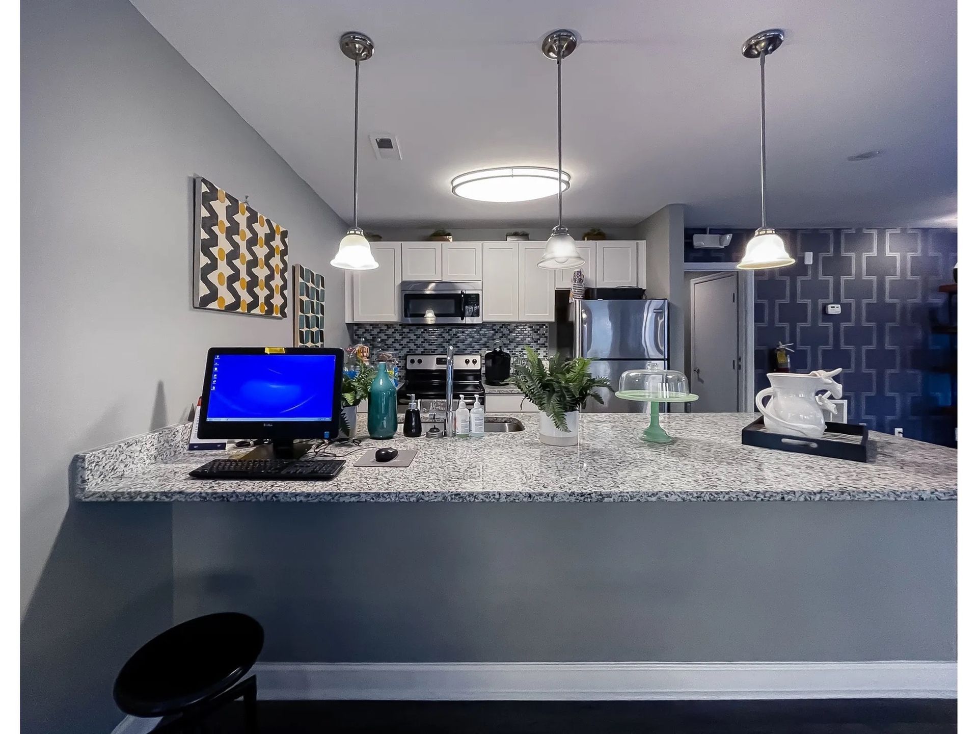 Modern apartment kitchen with granite island, pendant lights, and stainless steel appliances.