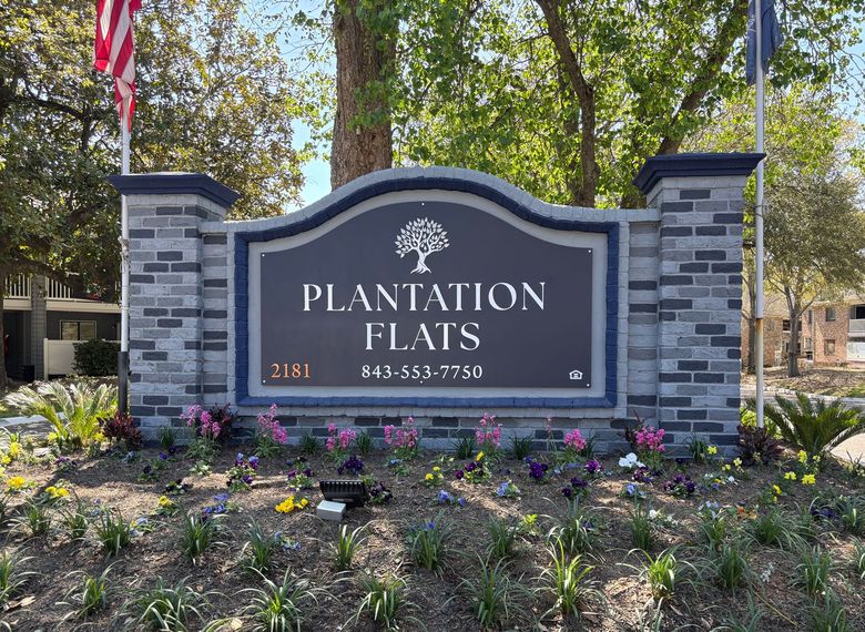 Community entrance sign reading Plantation Flats with stone pillars and landscaped flowers.