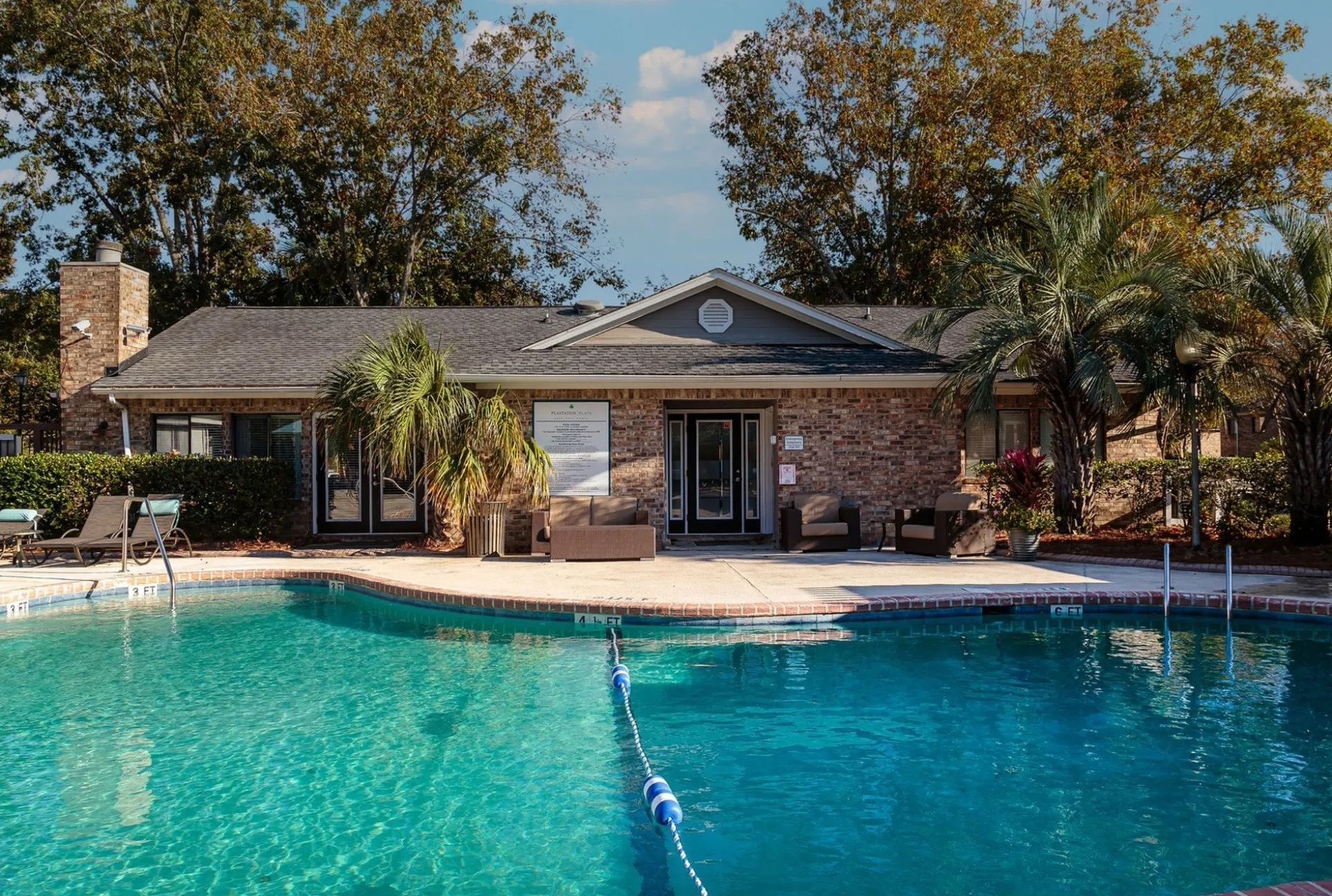 Outdoor apartment community pool with lounge seating, palm trees, and clear blue water.