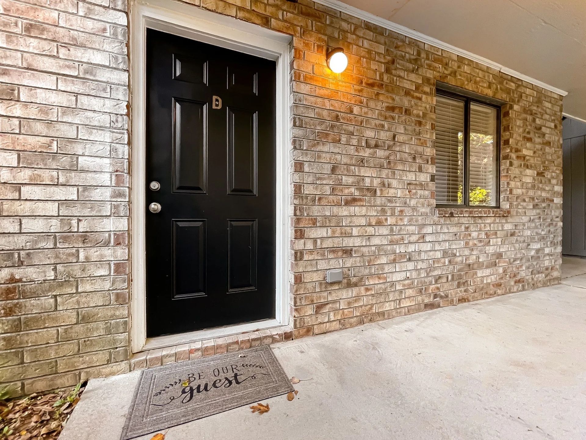 Brick exterior apartment entrance with a black door, a window, and a lit porch light.