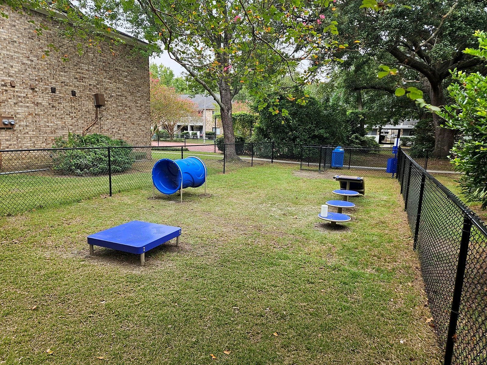 Fenced grassy playground area with blue tunnel structure and round platform steps.