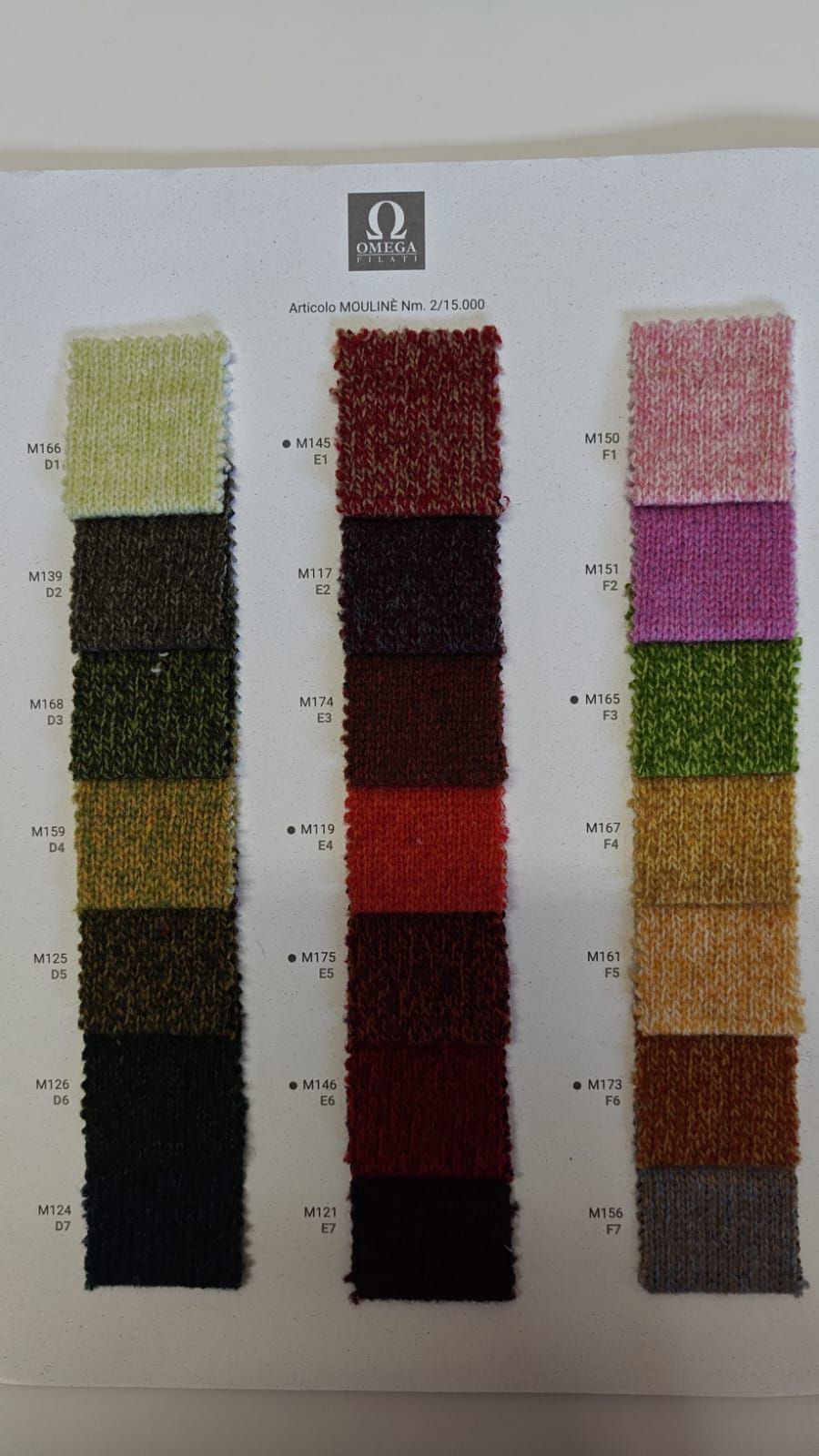 Muestras de tela en tonos verdes, rojos y rosas, dispuestas verticalmente sobre una tarjeta blanca 