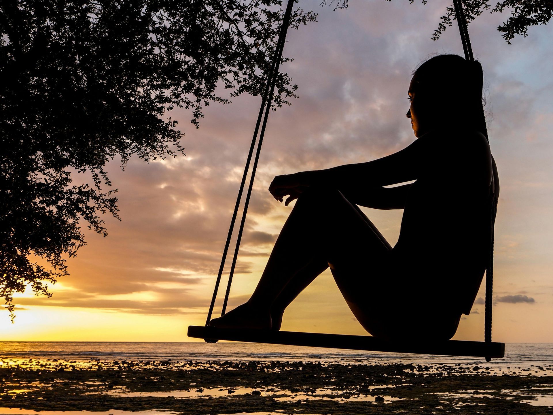 Une silhouette de femme assise sur une balançoire au coucher du soleil