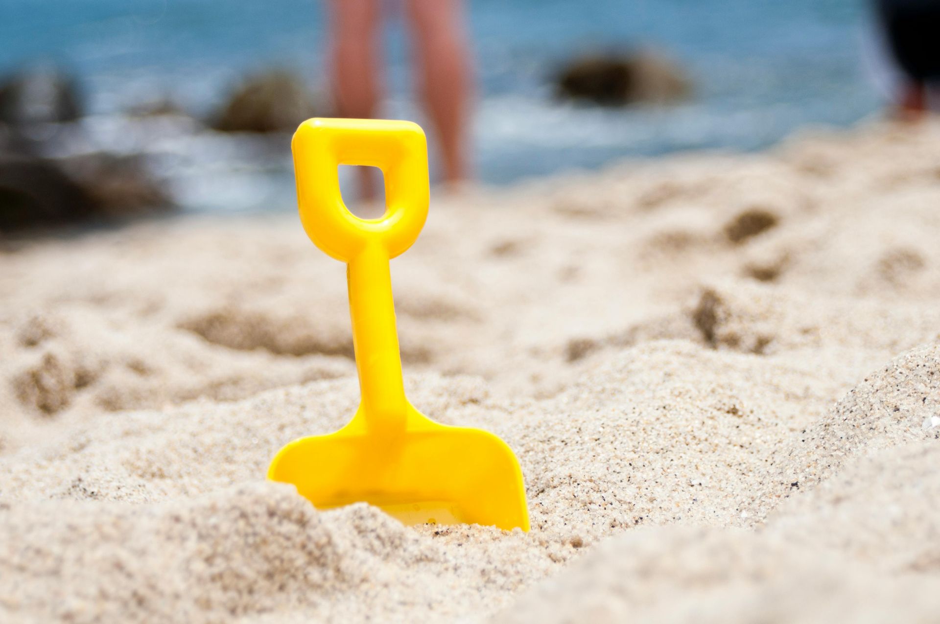Une pelle en plastique jaune est posée dans le sable sur la plage.