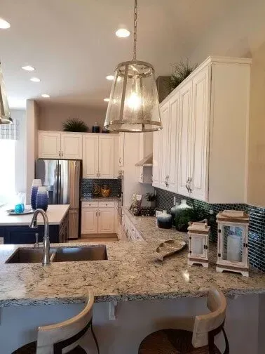 A kitchen with granite counter tops , white cabinets , a sink and a refrigerator.