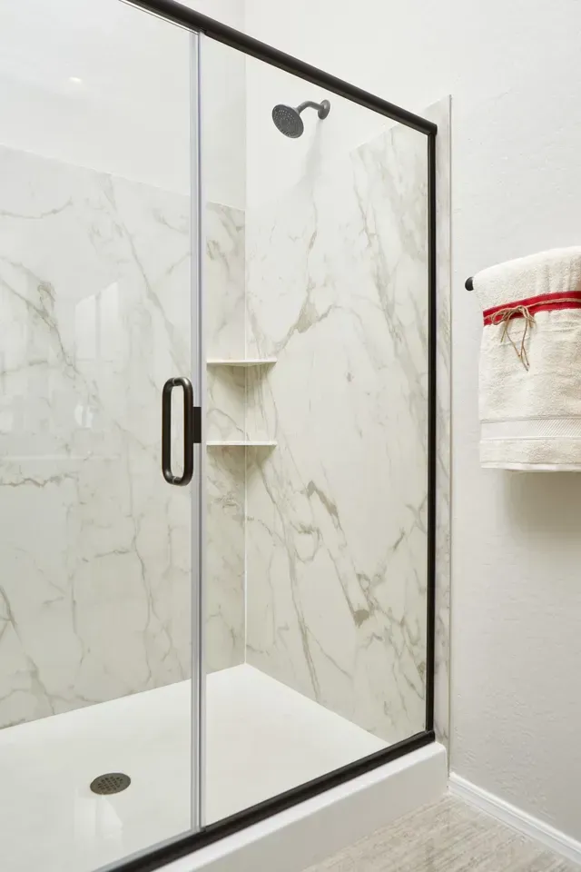 A bathroom with a walk in shower with a glass door and marble walls.