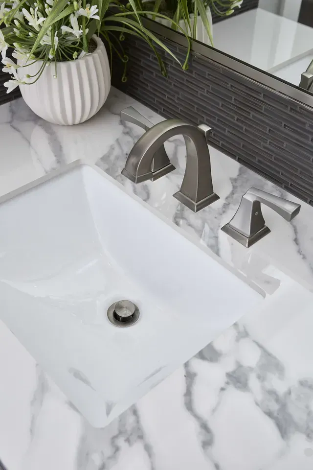 A bathroom sink with a vase of flowers on top of it.